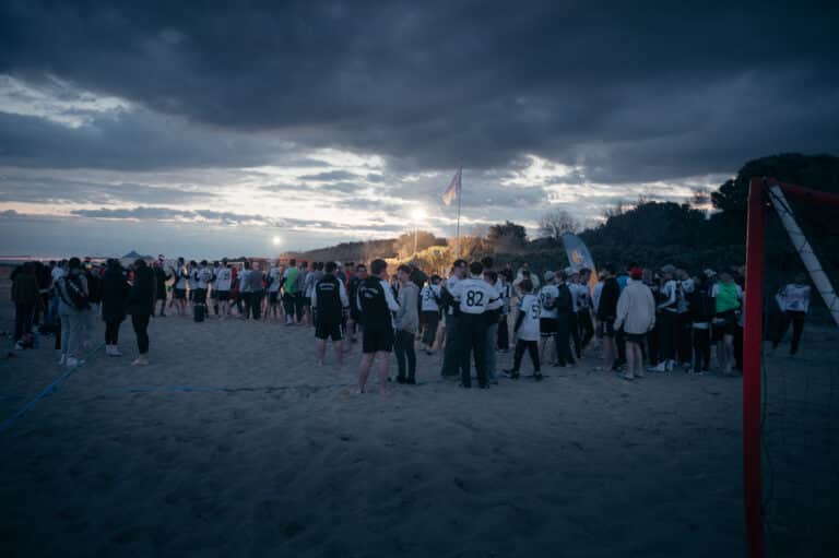 Many handball players gathered on a sandy beach at dusk.