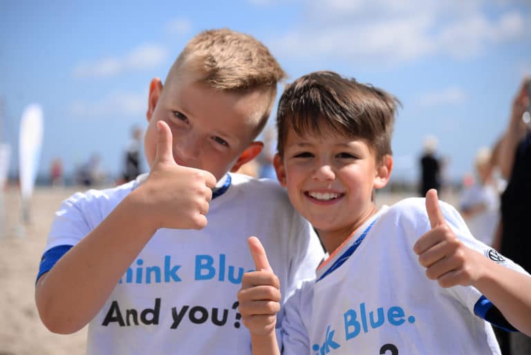 Two happy boys on a beach hold their thumbs up