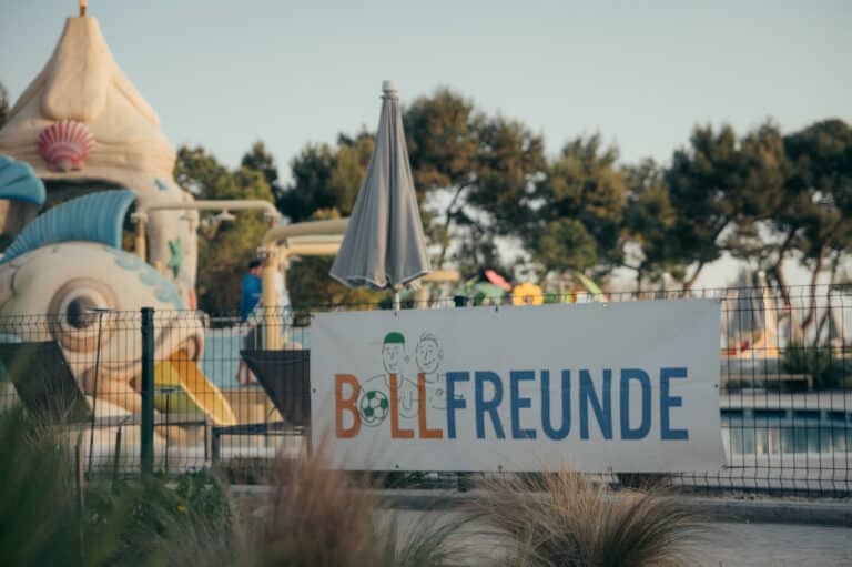 BALLFREUNDE Schild an Zaun vor einem Pool mit Rutsche und Liegen