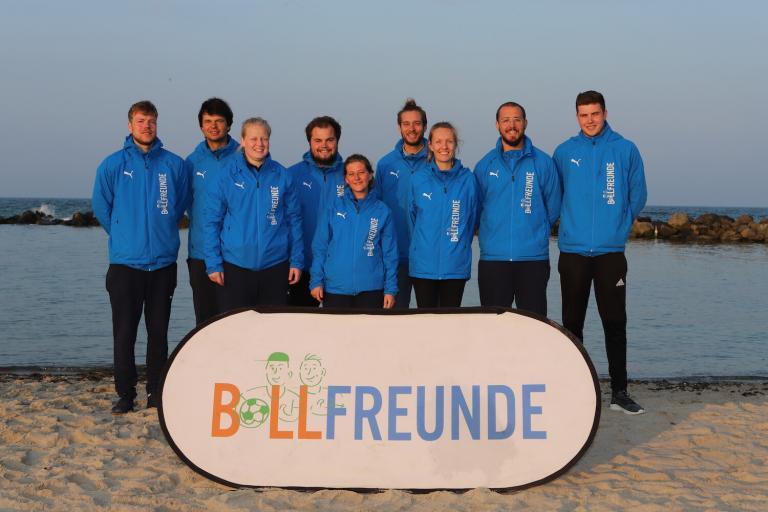 Il team Ballfreunde sulla spiaggia con lo striscione