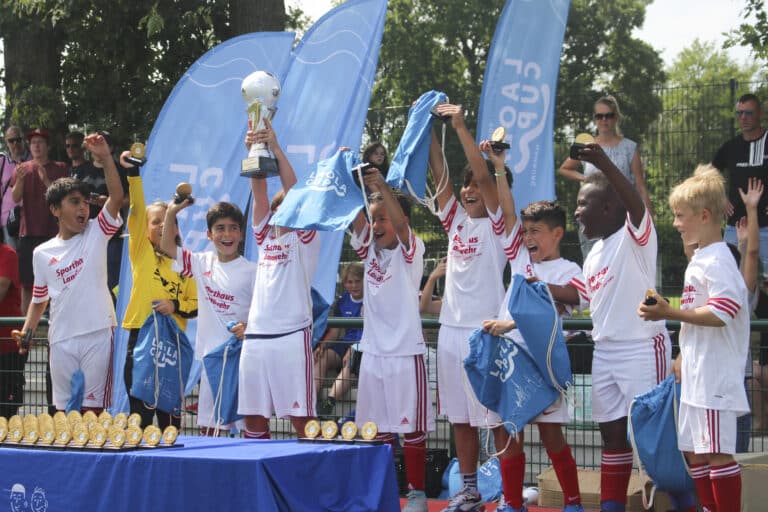 Verschillende kinderen in voetbaltenue houden trofeeën en tassen omhoog en vieren feest
