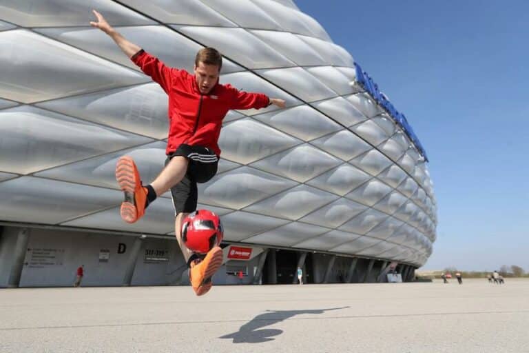 Football player outside a stadium does football trick