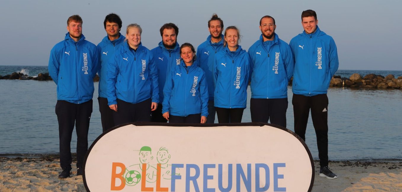 Il team Ballfreunde sulla spiaggia con lo striscione