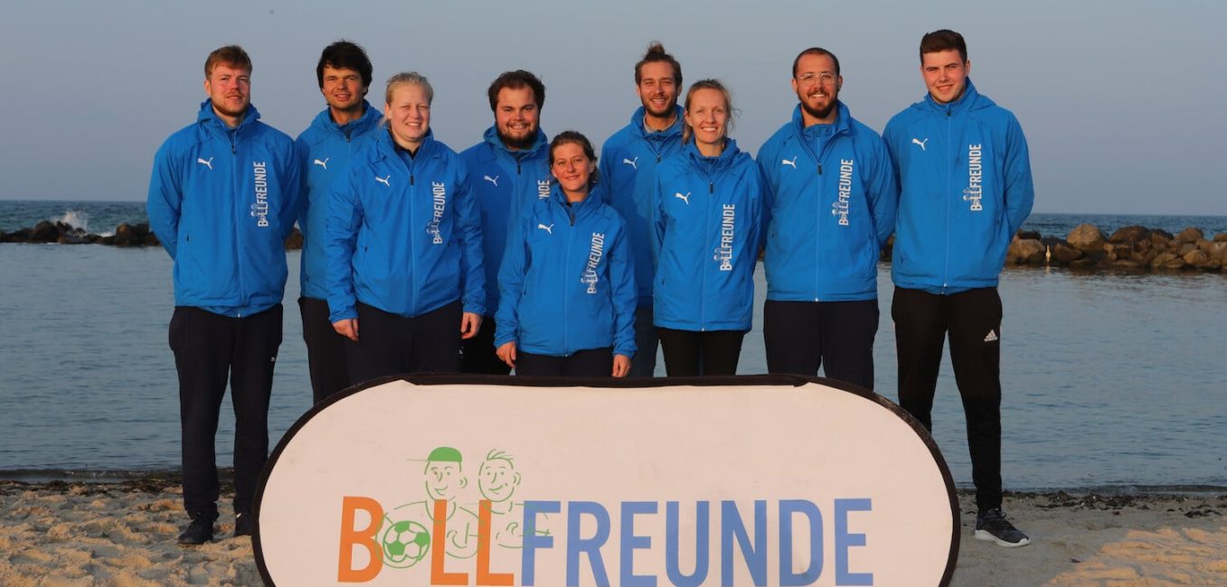 Team_Ballfriends Het Ballfreunde-team op het strand met spandoek