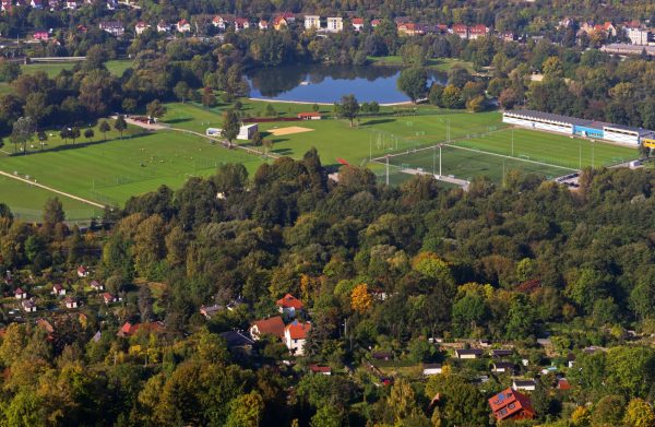 Dvě velká fotbalová hřiště u jezera a lesa s malou vesnicí.