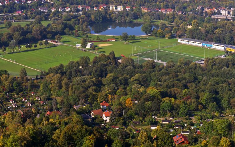 Dwa duże boiska do piłki nożnej położone obok jeziora i lasu z małą wioską.