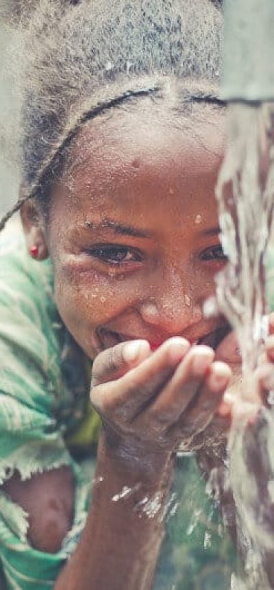Kleines Afrikanisches Mädchen ist glücklich beim Wasser trinken