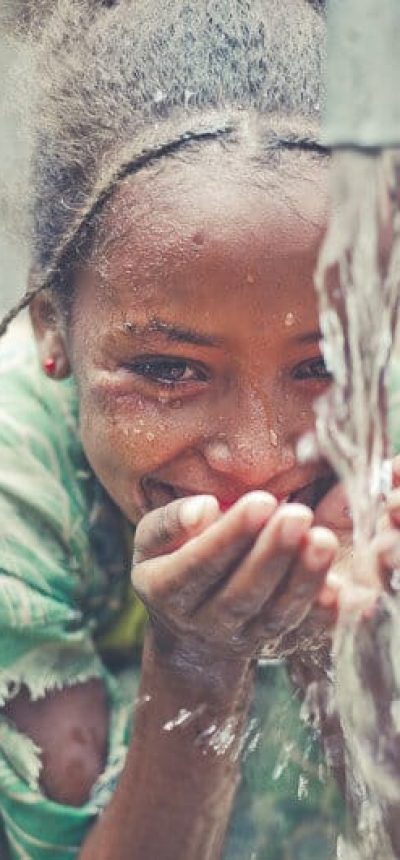 Liten afrikansk jente er glad for å drikke vann